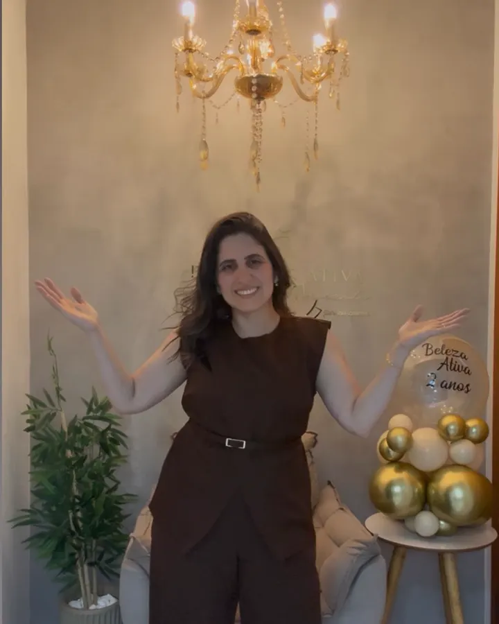Janaína de braços abertos sob um lustre dourado no spa
